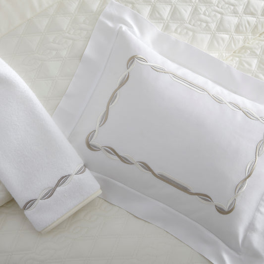 Home Treasures Cadence Embroidery in Mushroom, shown on a white Royal Sateen sham and Izmir terry towel, with an Abbey quilted backdrop in Ivory.