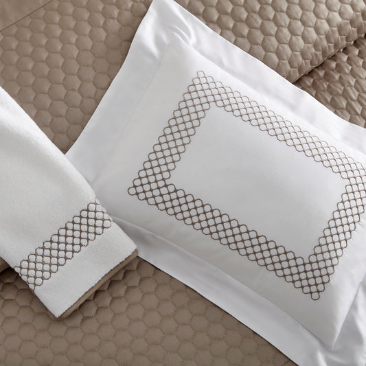 Home Treasures Margaux Embroidery in Mist Gray, shown on a white Royal Sateen sham and Izmir terry towel, with a Apiary quilted backdrop in Candlelight.