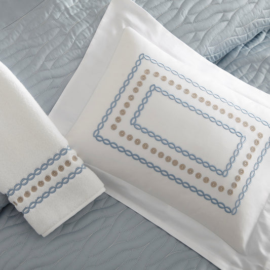 Home Treasures Mirabelle Embroidery in Coast, shown on a white Royal Sateen sham and Izmir terry towel, with a Napa quilted backdrop in Sion.