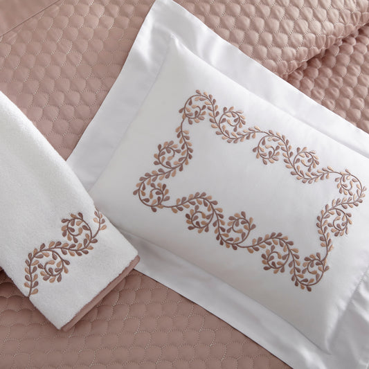 Home Treasures Olivia Embroidery in Rosewood, shown on a white Royal Sateen sham and Izmir terry towel, with a Trinity quilted backdrop in Dusty Rose.