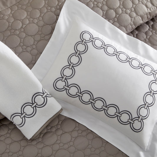 Home Treasures Rocco Embroidery in Stealth, shown on a white Royal Sateen sham and Izmir terry towel, with a Trinity quilted backdrop in Mist Gray.